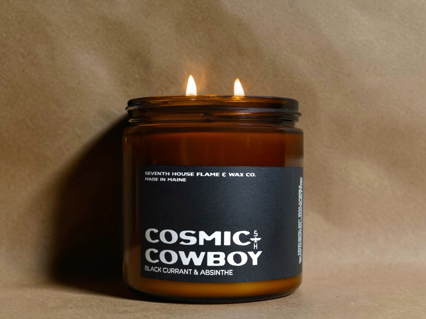Candle in a brown jar labeled 'Cosmic Cowboy' with a dark label on a beige background