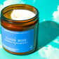 Candle in an amber jar with a blue label on a cloud-themed background