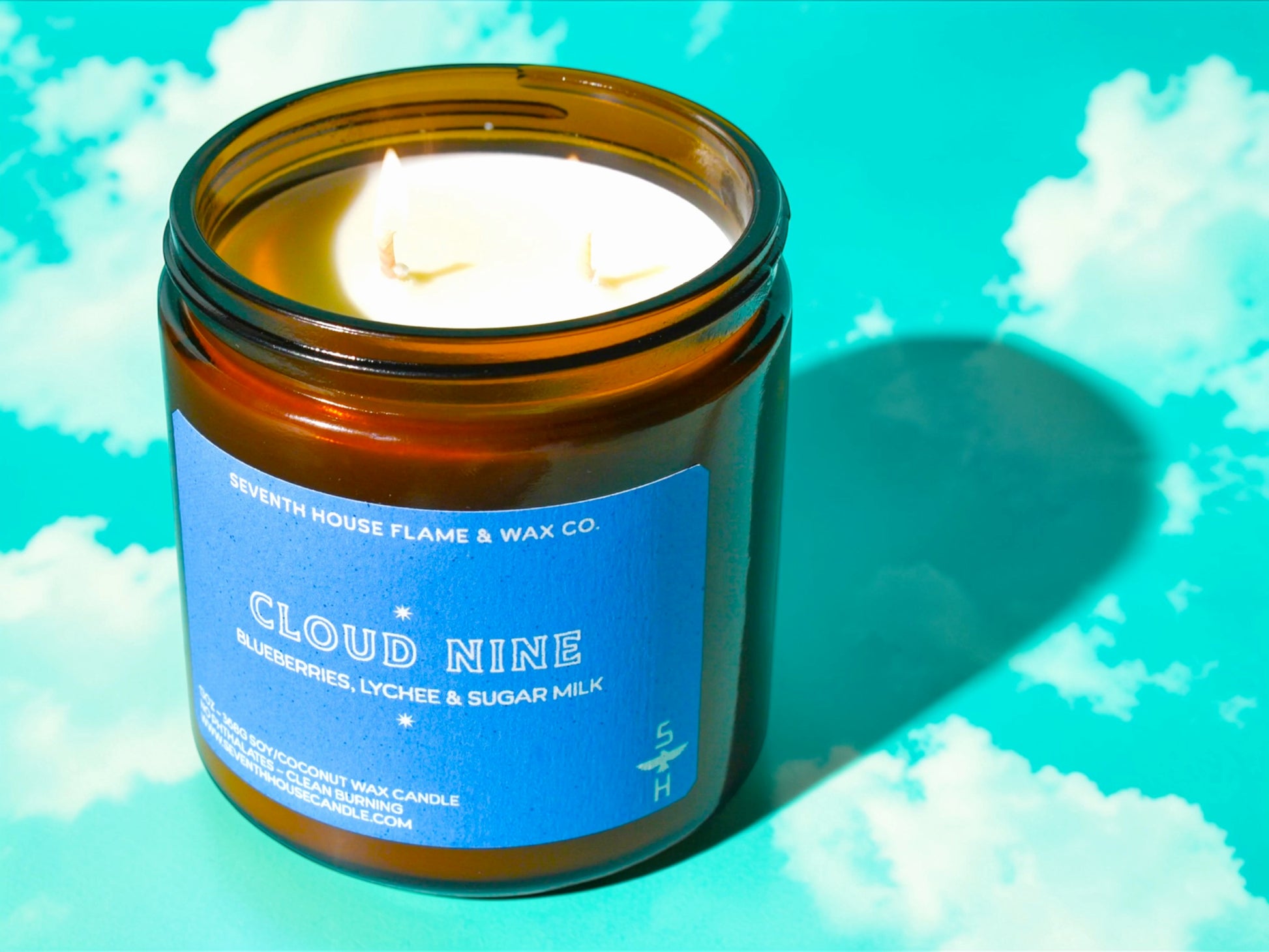 Candle in an amber jar with a blue label on a cloud-themed background