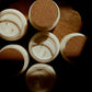 Five open white candles with cork stoppers arranged on a dark wooden surface under dramatic warm lighting.