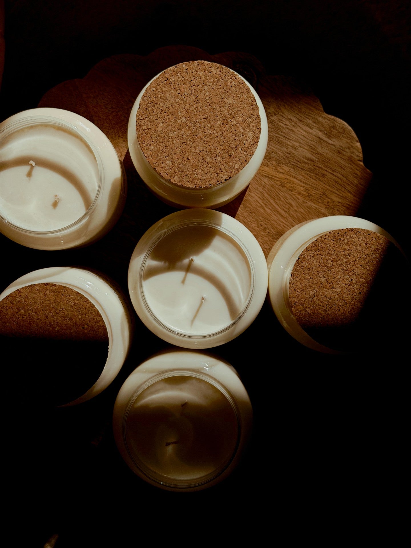 Five open white candles with cork stoppers arranged on a dark wooden surface under dramatic warm lighting.