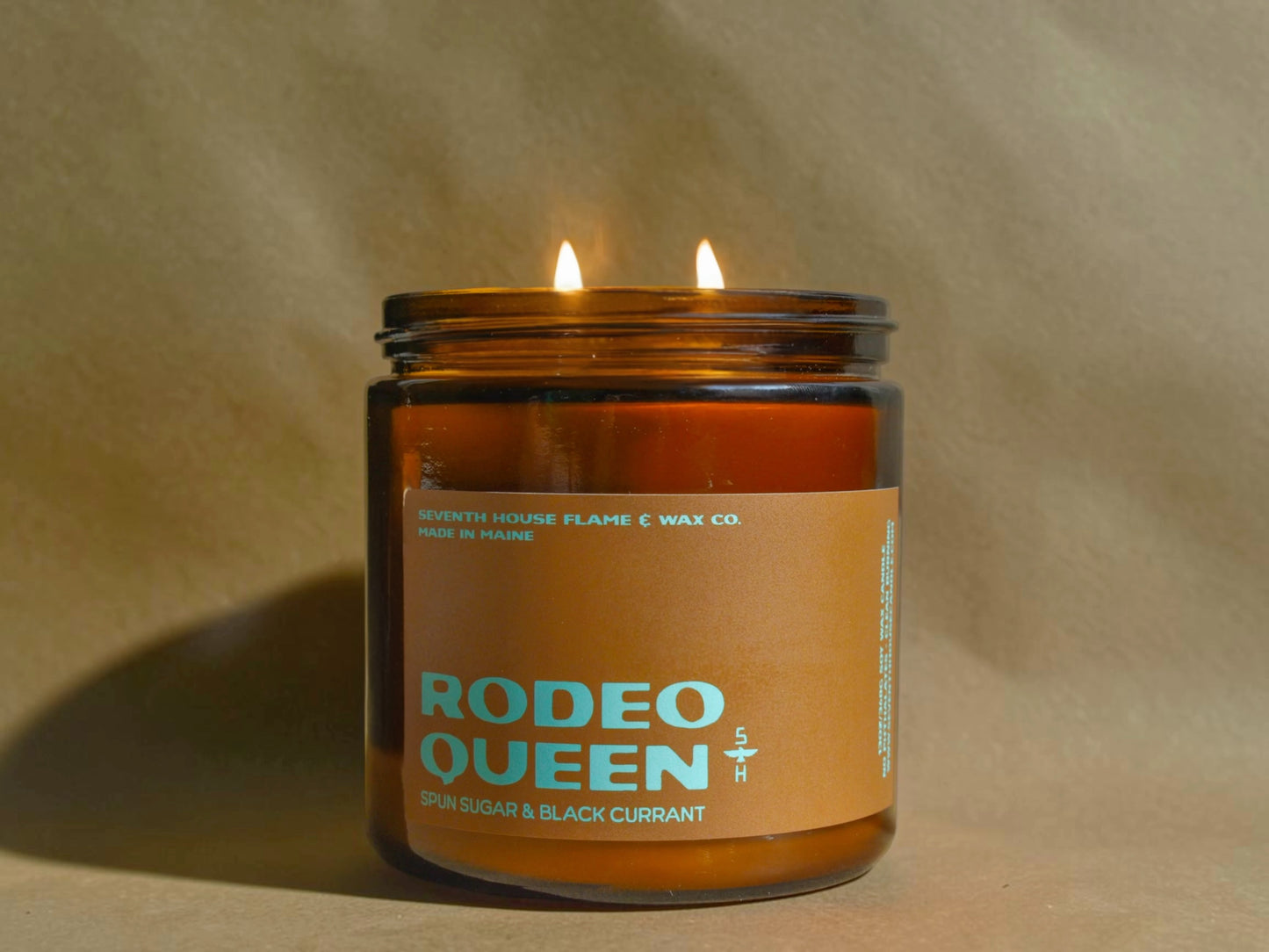 Candle in a glass jar labeled 'Rodeo Queen' on a beige background