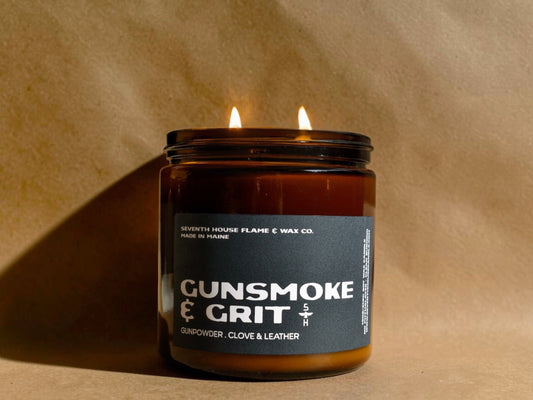 Candle in a jar labeled 'Gunsmoke & Grit' on a beige background