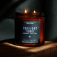 A lit amber glass jar candle labeled 'Twilight Trail' by Seventh House Candle, placed on a wooden surface against a dark draped background.