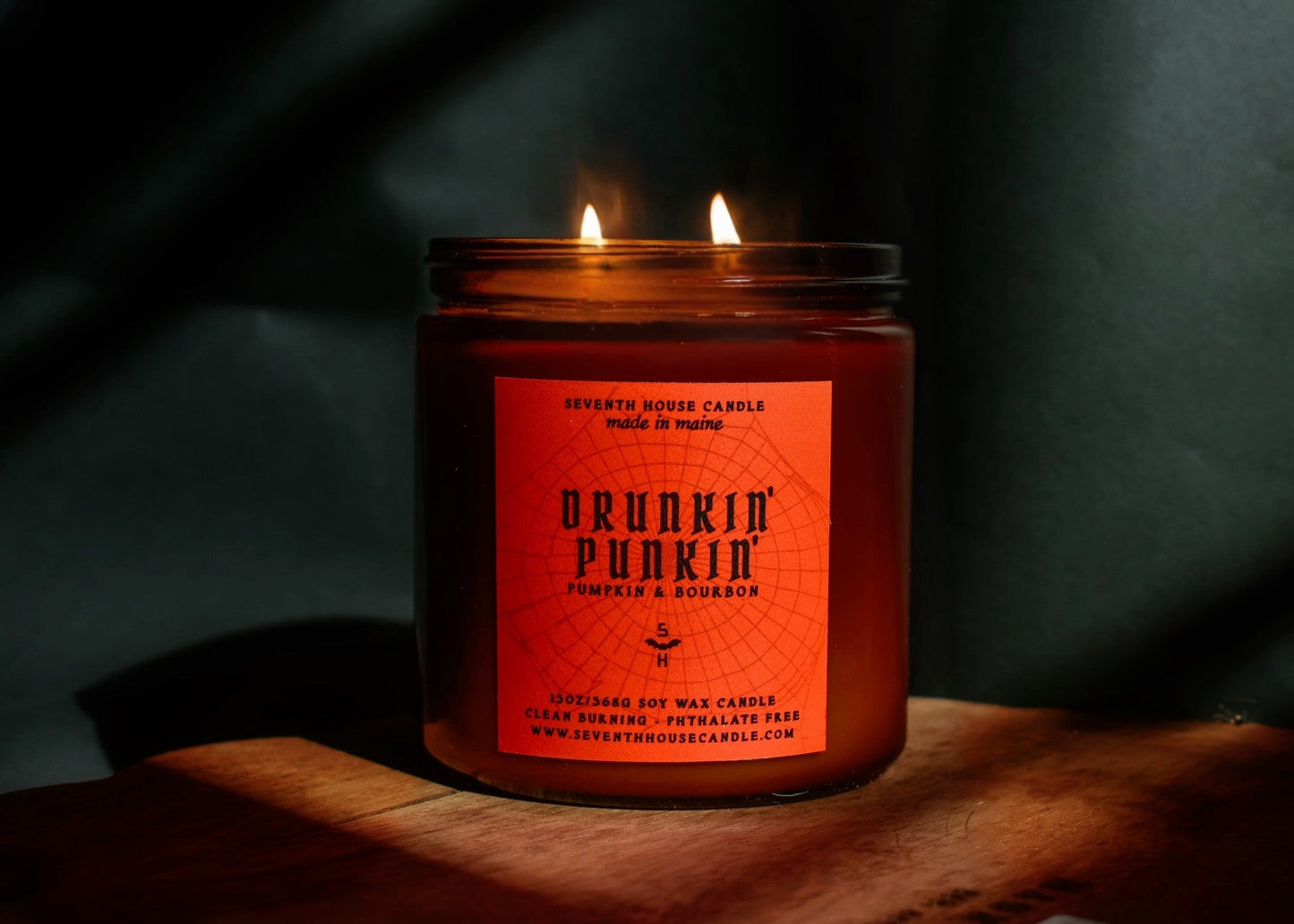 A lit amber glass jar candle with a red-orange label reading 'Bunkin' Punkin' and 'Pimpelip & Research,' set on a wooden surface against a dark draped background.