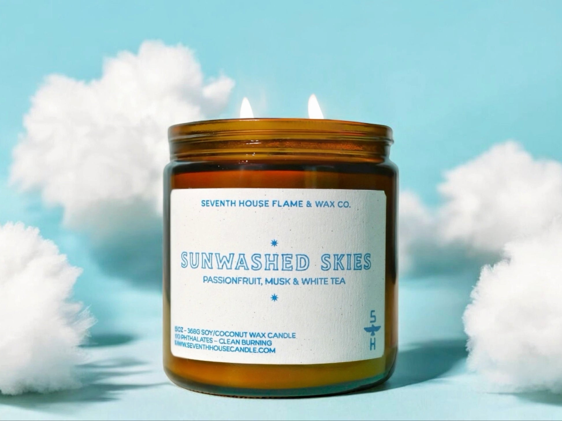Candle jar labeled 'Sunwashed Skies' by Seventh House Flame & Wax Co. on a light blue background with white fluffy elements.