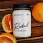 Candle jar labeled 'Rooted' with oranges on a wooden surface
