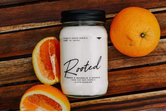 Candle jar labeled 'Rooted' with oranges on a wooden surface