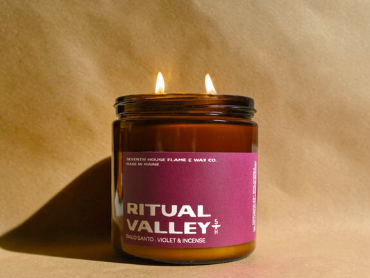 Candle in a brown jar with a purple label on a beige background