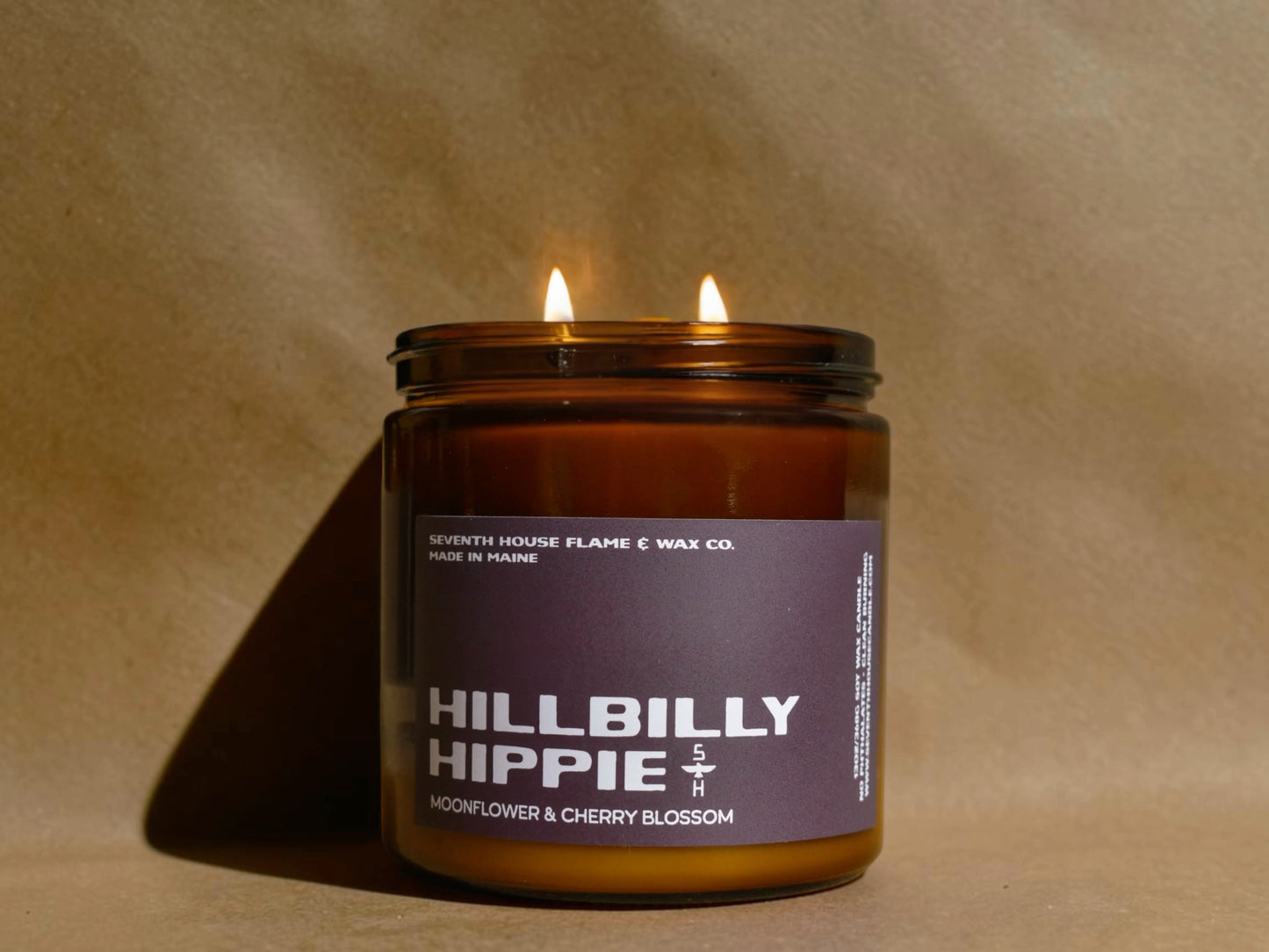 Candle in an amber jar labeled 'Hillbilly Hippie' on a beige background