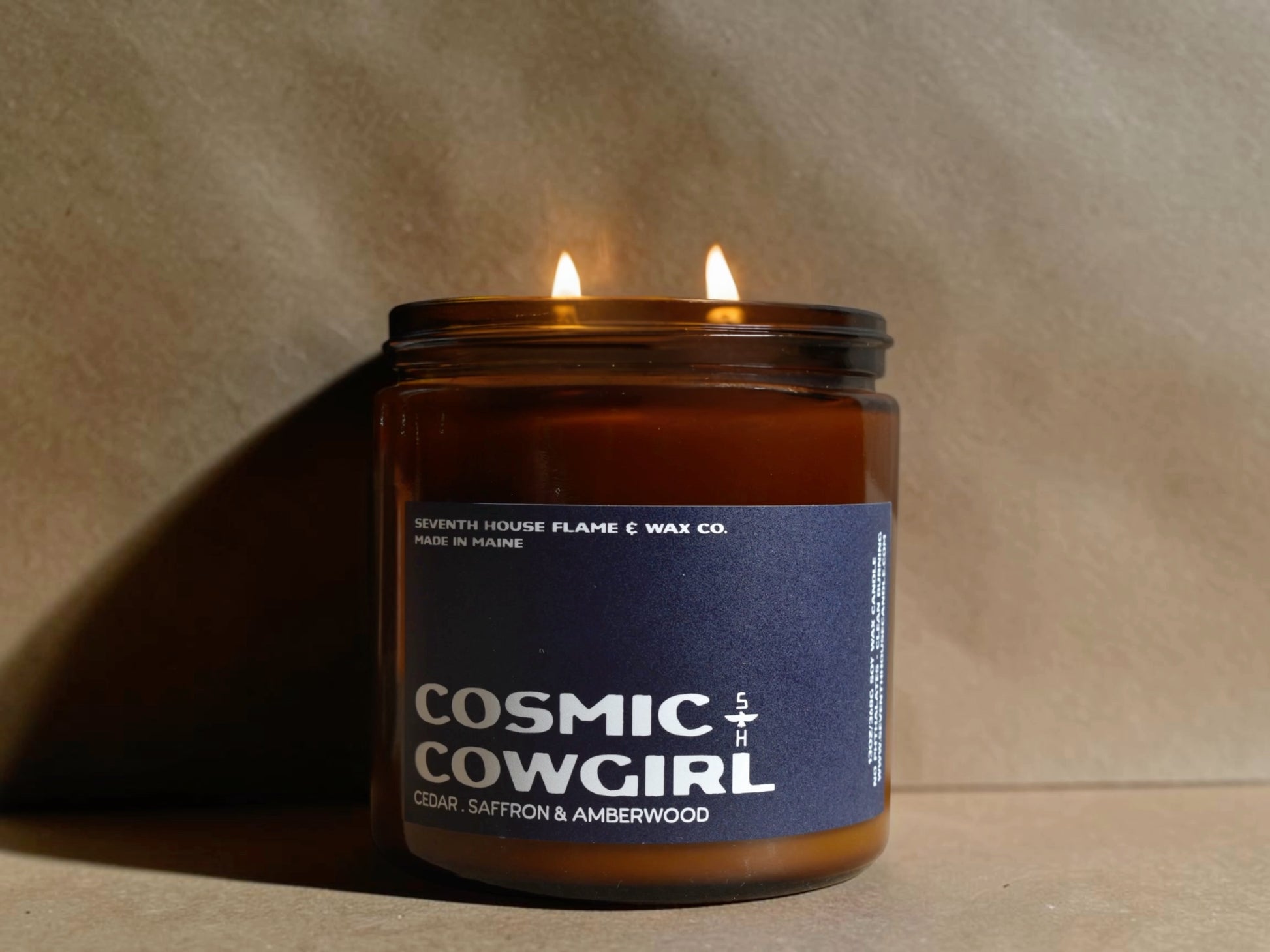 Candle in a jar labeled 'Cosmic Cowgirl' with a blue label on a beige background