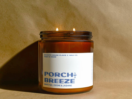 Candle in a glass jar labeled 'Porch Breeze' on a beige background